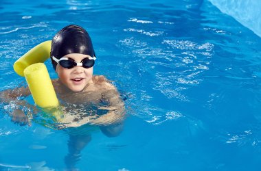 Junge auf Poolnoodle mit Schwimmbrille im Wasser